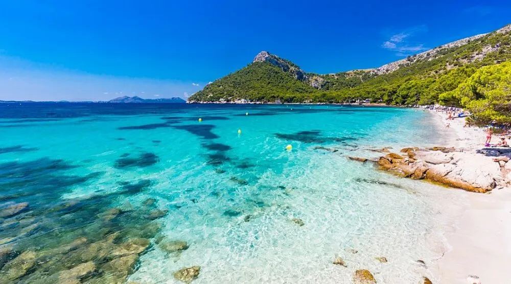 Clear shallow water at Formentor beach with a green mountain behind