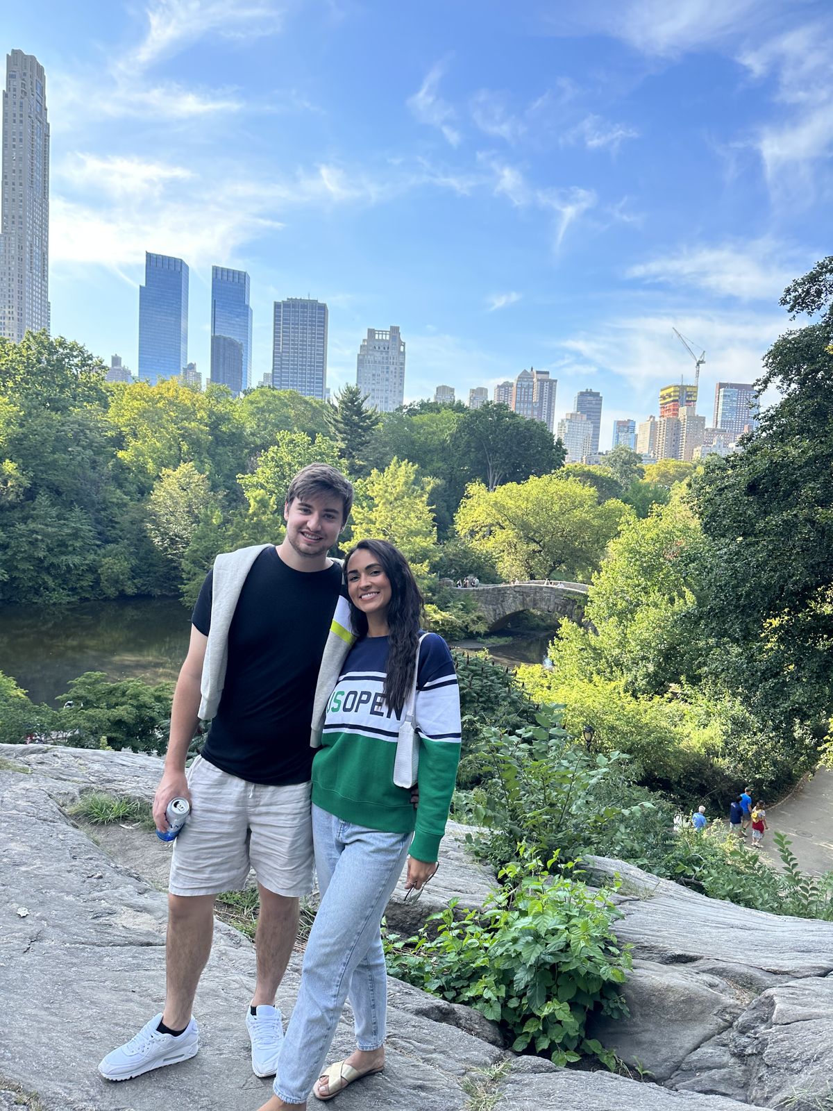 The couple on rocks in a park with skyscrapers behind