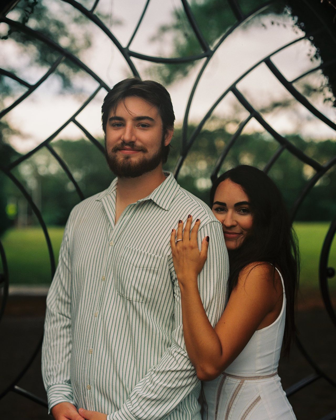 Jessica resting her hand on Patrick’s shoulder in front of an iron gate
